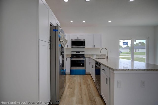 kitchen featuring appliances with stainless steel finishes, light stone counters, sink, light hardwood / wood-style flooring, and white cabinets