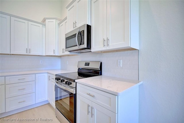 kitchen with appliances with stainless steel finishes, tasteful backsplash, white cabinetry, light stone counters, and light wood-type flooring