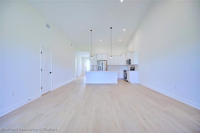 unfurnished living room featuring a towering ceiling and light hardwood / wood-style flooring