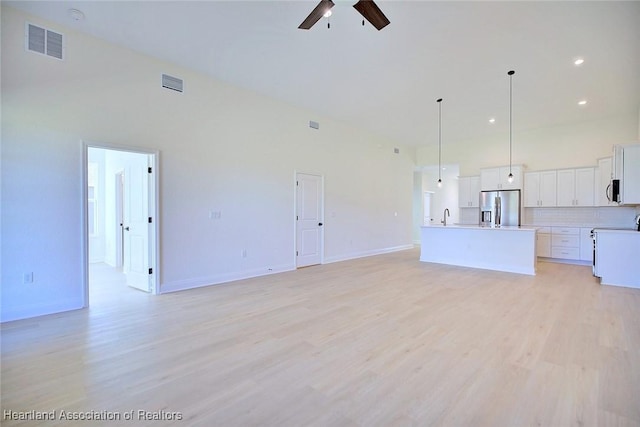 unfurnished living room featuring a high ceiling, sink, ceiling fan, and light hardwood / wood-style flooring