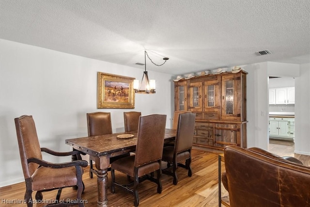 dining room featuring a chandelier, light hardwood / wood-style floors, and a textured ceiling