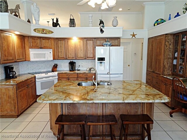 kitchen with a breakfast bar, white appliances, backsplash, a kitchen island with sink, and sink