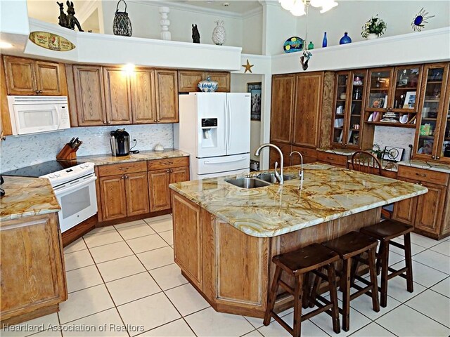 kitchen with a towering ceiling, white appliances, sink, a breakfast bar area, and an island with sink