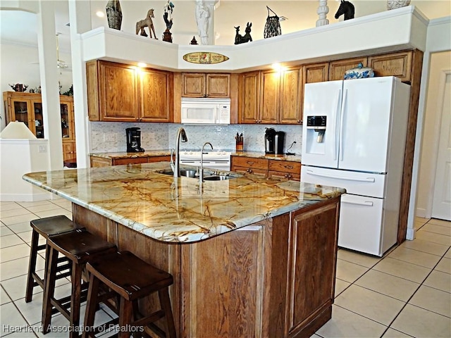 kitchen with white appliances, light tile patterned flooring, brown cabinets, and a sink