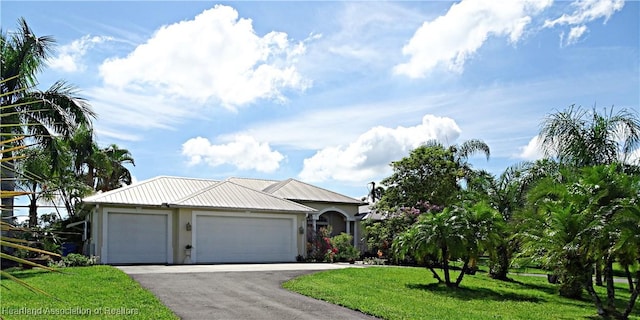 ranch-style house with stucco siding, a front yard, an attached garage, driveway, and metal roof