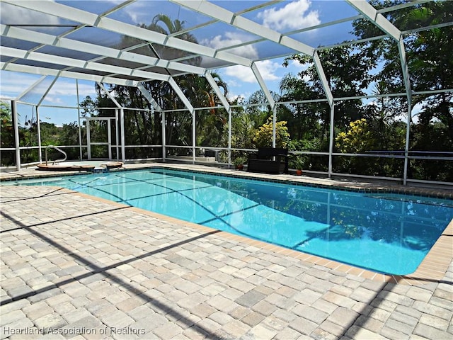 view of pool featuring a patio area, glass enclosure, view of wooded area, and a pool with connected hot tub