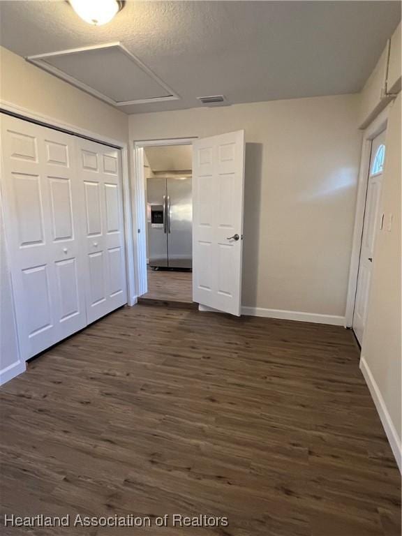 unfurnished bedroom featuring stainless steel refrigerator with ice dispenser, dark hardwood / wood-style floors, a closet, and a textured ceiling