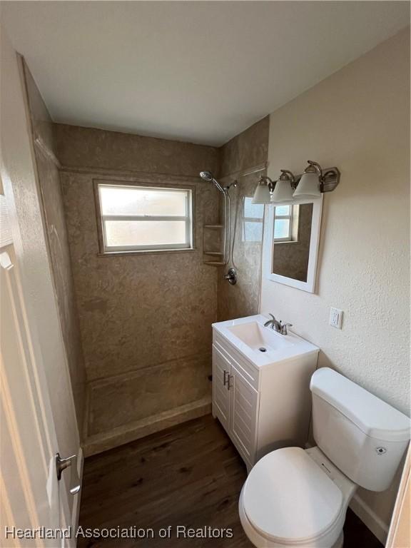 bathroom with hardwood / wood-style flooring, vanity, tiled shower, and toilet