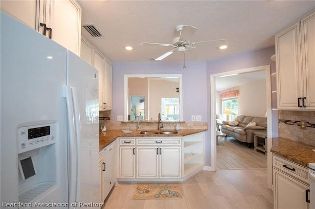 kitchen with white refrigerator with ice dispenser, white cabinets, dark stone counters, and sink