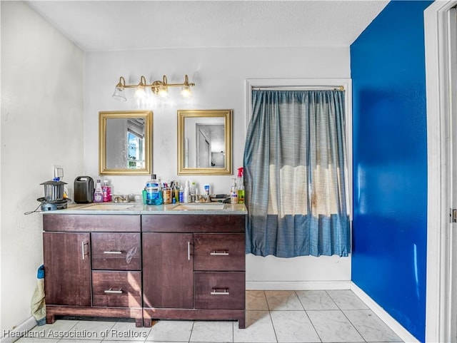 bathroom with baseboards, double vanity, a sink, and tile patterned floors