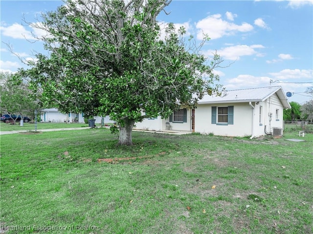 view of front of house with central AC, metal roof, a front lawn, and stucco siding