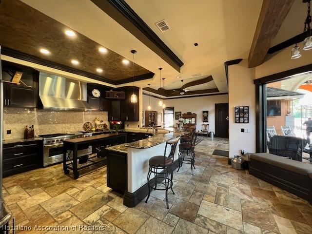 2230 Lake Ariana Blvd, Auburndale, FL 33823 - kitchen featuring wall chimney range hood, stone tile flooring, a breakfast bar, stainless steel range, and tasteful backsplash