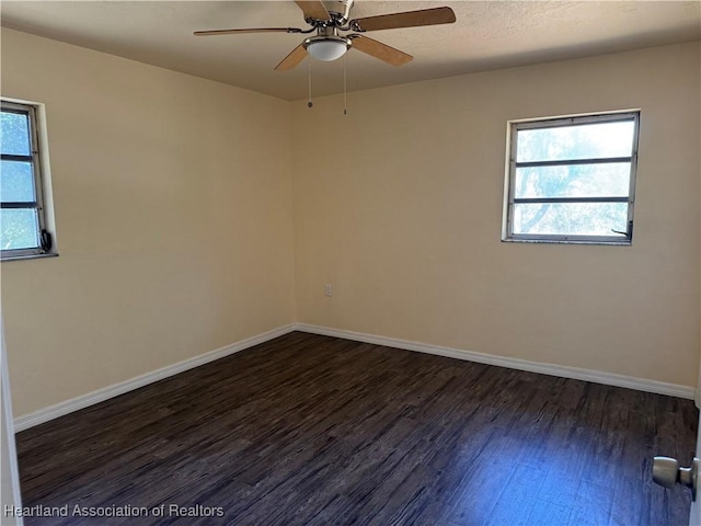 unfurnished room featuring dark wood-style flooring, ceiling fan, plenty of natural light, and baseboards
