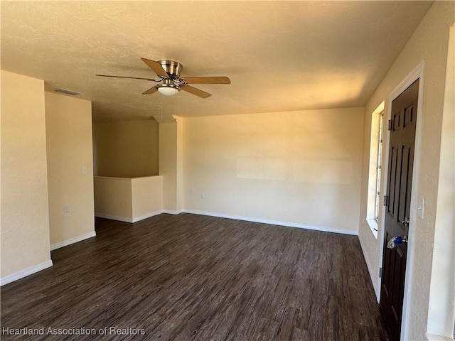 empty room featuring dark wood-style flooring, baseboards, visible vents, and ceiling fan