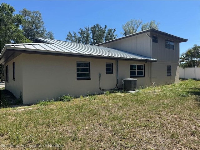 rear view of property featuring a standing seam roof, cooling unit, a yard, stucco siding, and fence