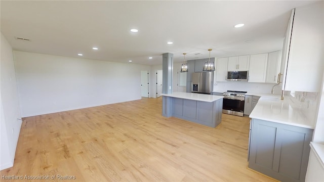 kitchen with light wood-type flooring, stainless steel appliances, white cabinets, a center island, and hanging light fixtures