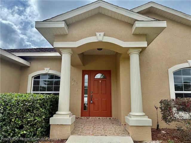 view of exterior entry with a shingled roof and stucco siding