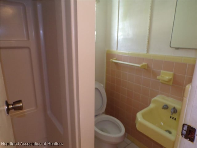 bathroom featuring toilet, tile walls, and sink