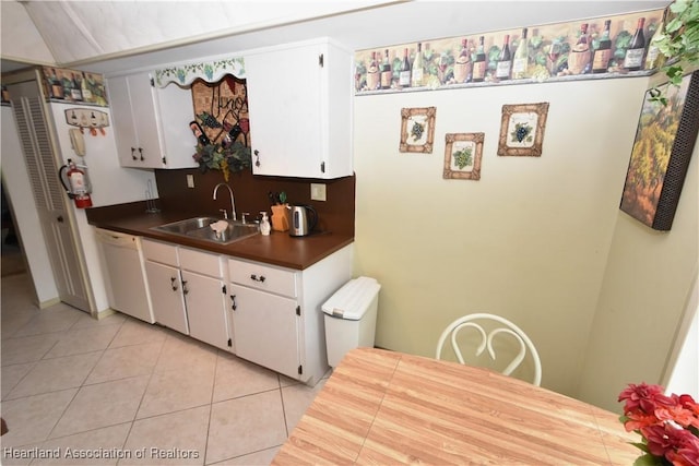 kitchen with white dishwasher, white cabinets, light tile patterned floors, and sink