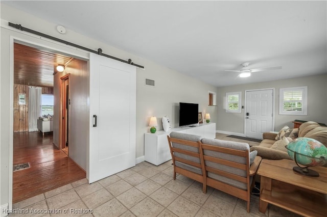 living area with light tile patterned floors, a barn door, visible vents, and a ceiling fan