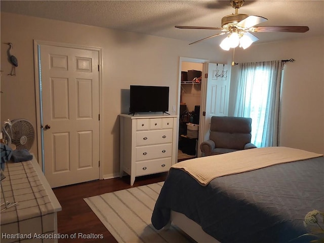 bedroom with a closet, a ceiling fan, a spacious closet, a textured ceiling, and dark wood finished floors