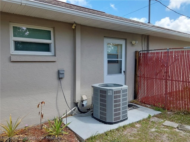 exterior details with stucco siding, central air condition unit, and fence