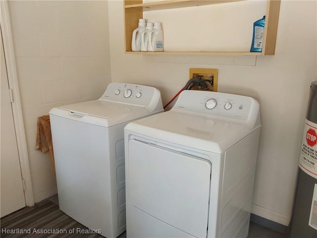 laundry room featuring water heater, concrete block wall, dark wood-style floors, laundry area, and independent washer and dryer