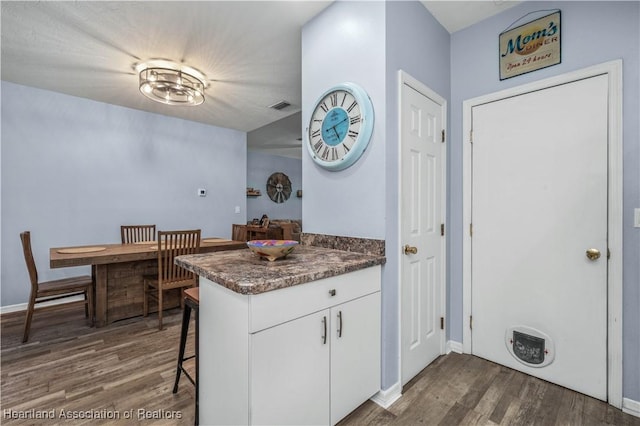 kitchen featuring dark hardwood / wood-style flooring, kitchen peninsula, white cabinets, and a breakfast bar