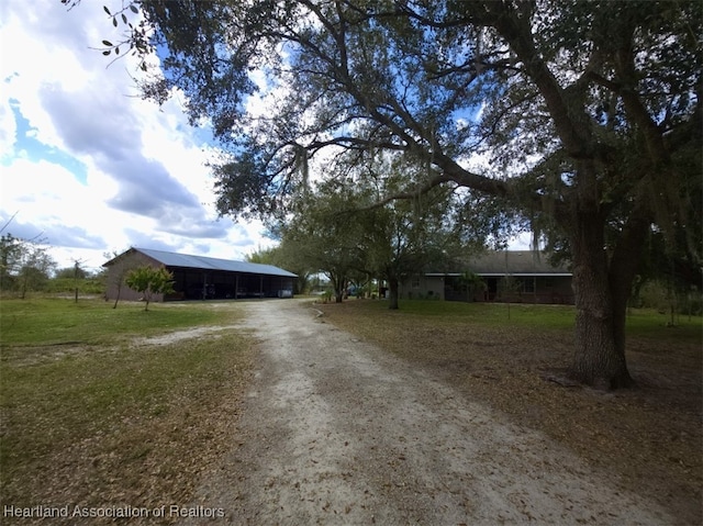 view of front of home featuring dirt driveway, a carport, a front lawn, and a pole building