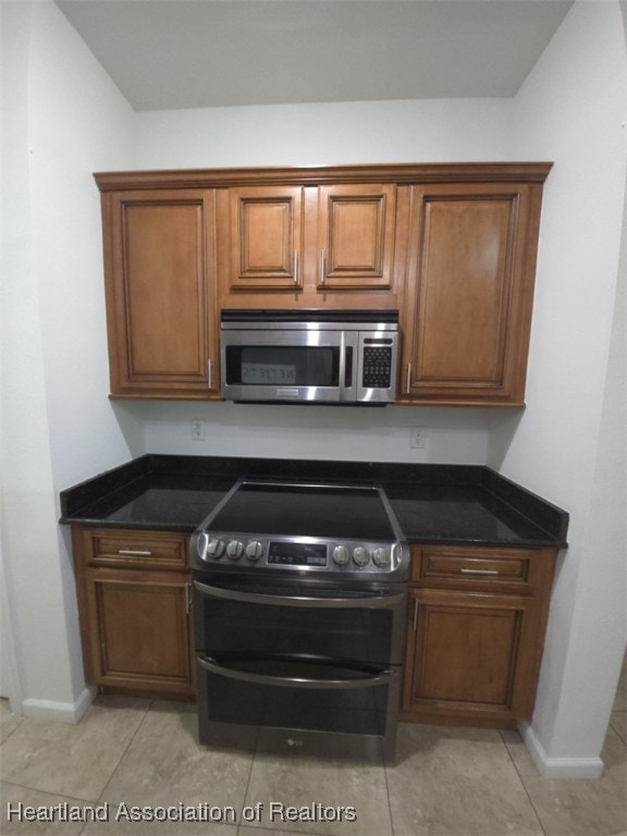 kitchen with baseboards, appliances with stainless steel finishes, brown cabinetry, and dark stone countertops