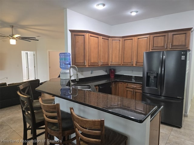 kitchen with a breakfast bar, dark stone countertops, a peninsula, black appliances, and a sink