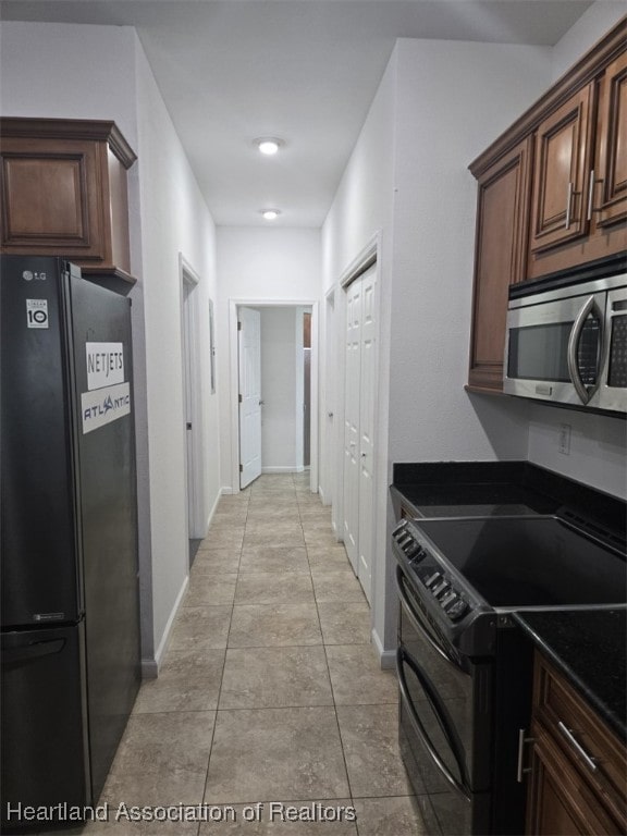 kitchen featuring dark countertops, black appliances, light tile patterned floors, and baseboards