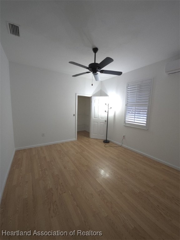 unfurnished bedroom with light wood finished floors, a wall mounted AC, visible vents, and baseboards