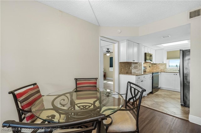 dining room featuring ceiling fan, sink, a textured ceiling, and light wood-type flooring