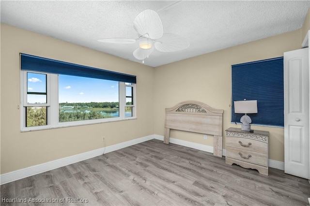 bedroom featuring ceiling fan, a water view, a textured ceiling, and light hardwood / wood-style flooring