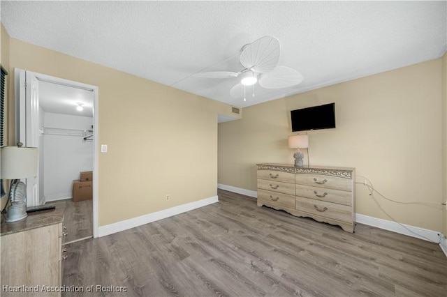 bedroom featuring hardwood / wood-style floors, a walk in closet, ceiling fan, a textured ceiling, and a closet