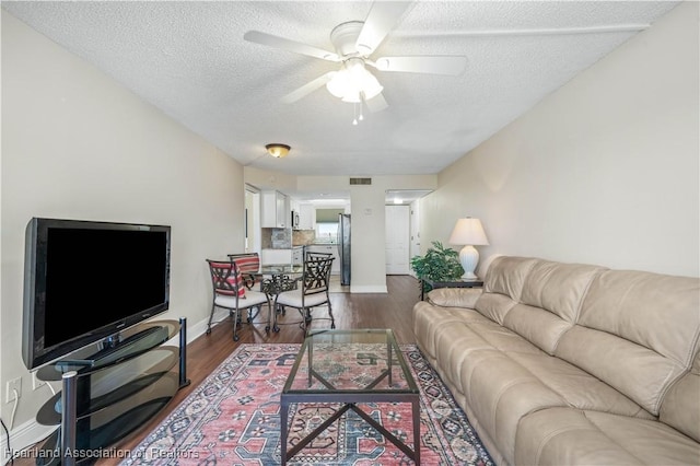 living room with ceiling fan, dark wood-type flooring, and a textured ceiling