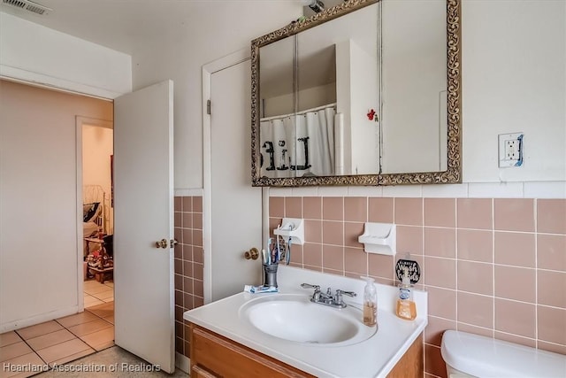 bathroom with tile patterned floors, vanity, toilet, and tile walls