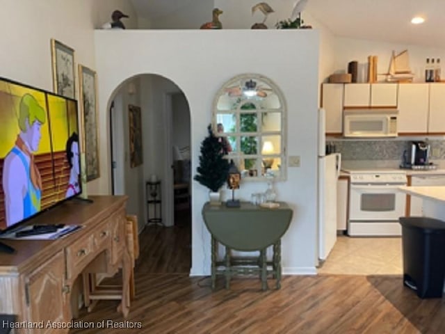 kitchen with backsplash, vaulted ceiling, white appliances, and light wood-type flooring