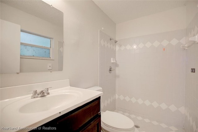 bathroom featuring tiled shower, vanity, a textured ceiling, and toilet