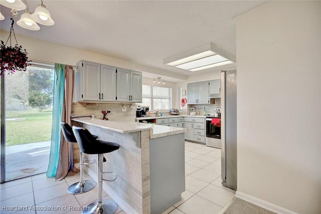 kitchen with electric range, light tile patterned floors, tasteful backsplash, kitchen peninsula, and a breakfast bar area