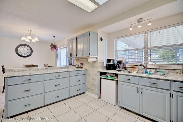 kitchen featuring gray cabinetry, sink, hanging light fixtures, light tile patterned floors, and a chandelier