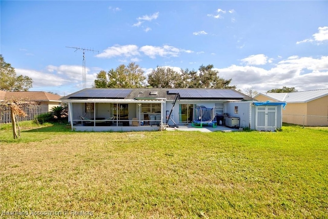 rear view of house with solar panels, a sunroom, a trampoline, a shed, and a lawn