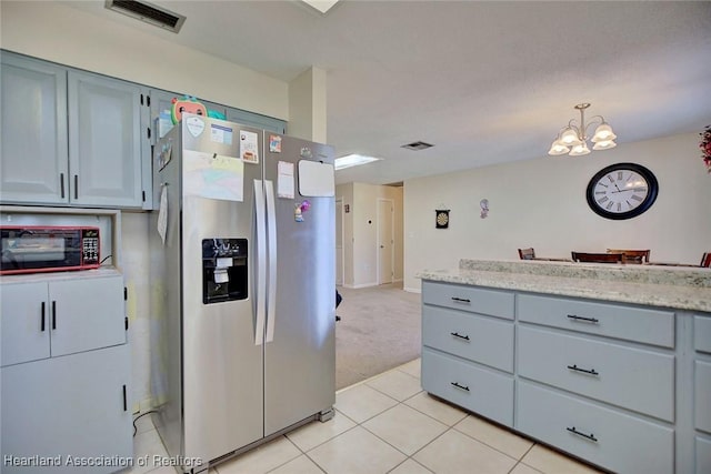 kitchen with stainless steel refrigerator with ice dispenser, hanging light fixtures, a notable chandelier, light tile patterned flooring, and light stone counters