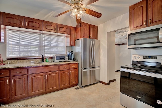 kitchen with sink, ceiling fan, light stone counters, and stainless steel appliances