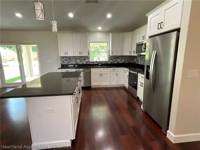 kitchen featuring stainless steel appliances, sink, pendant lighting, white cabinets, and a center island