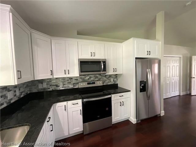 kitchen featuring stainless steel appliances, tasteful backsplash, dark stone countertops, vaulted ceiling, and white cabinets