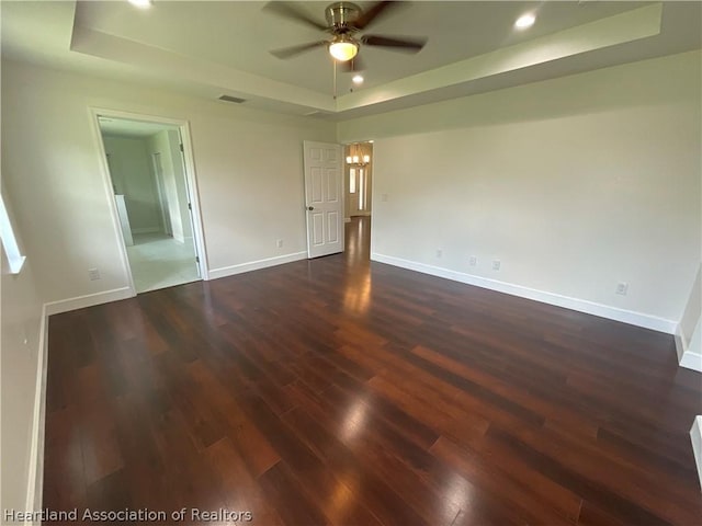 unfurnished room featuring a tray ceiling, ceiling fan, and dark hardwood / wood-style flooring