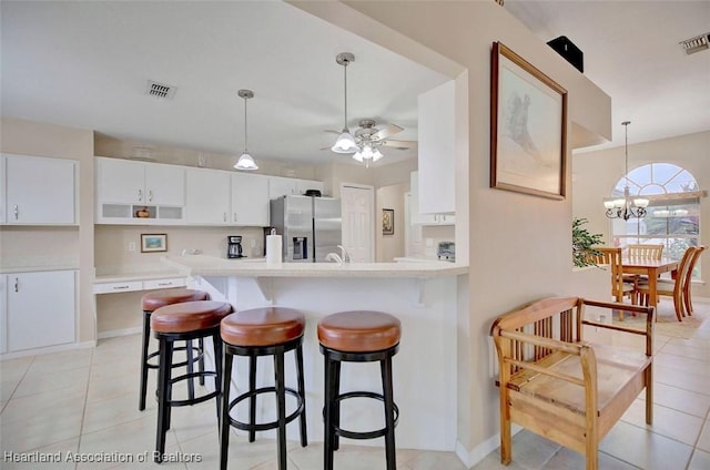 kitchen featuring pendant lighting, stainless steel fridge, ceiling fan with notable chandelier, and white cabinets