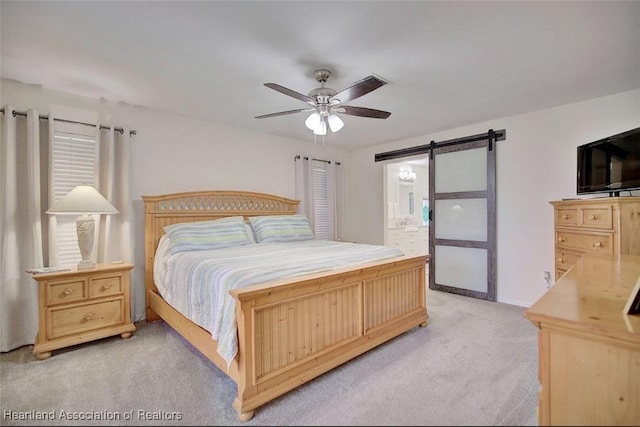 carpeted bedroom featuring ensuite bath, a barn door, and ceiling fan